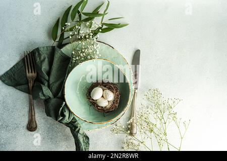 Blick von oben auf einen Osterplatz mit Ostereiern in einem Vogelnest, Roskuszweigen und weißen Gypsophila-Blumen Stockfoto