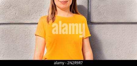 Unerkennbare lächelnde, glückliche blonde Frau im gelb-orangefarbenen T-Shirt auf grauem Hintergrund Mockup-freundlicher Kopierbereich für Design und Text Urban Stockfoto