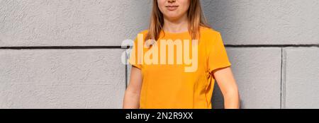 Nicht wiedererkennbare blonde Frau im Jahrtausendalter im gelb-orangefarbenen T-Shirt mit grauem Hintergrund Mockup-freundlicher Kopierbereich für Design und Text Urban Clot Stockfoto