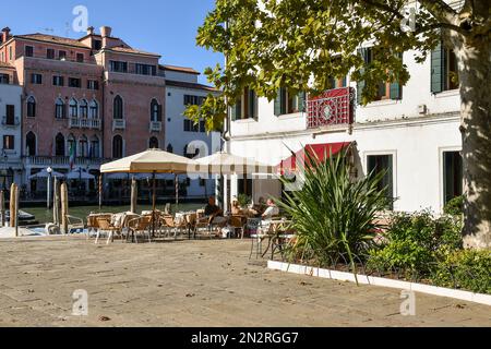 Touristen in einem Straßencafé mit Blick auf den Canale Granale Grande im Campo San Simeone Grande, einem kleinen Platz im Sestiere von Santa Croce, Venedig, Italien Stockfoto