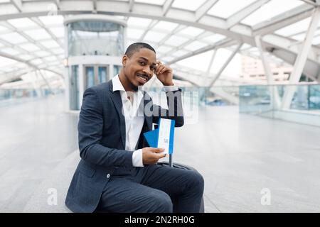 Glücklicher Schwarzer Geschäftsmann, Der Mit Pass Und Tickets In Der Hand Am Flughafen Posiert Stockfoto