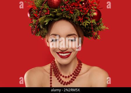 Schöne junge Frau mit Weihnachtskranz auf rotem Hintergrund Stockfoto