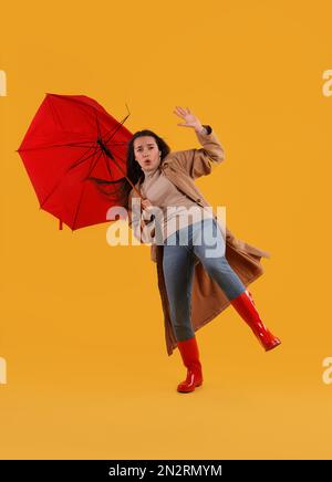 Emotionale Frau mit Regenschirm, der von Windböen auf gelbem Hintergrund gefangen wurde Stockfoto