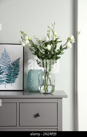 Komposition mit Eustoma-Blüten in Glasvase auf grauen Schränken im Innenbereich Stockfoto