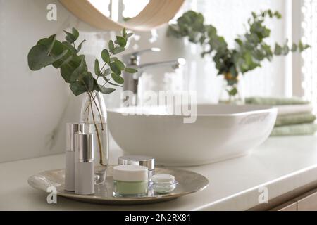 Frische Eukalyptusäste und Kosmetikprodukte auf der Arbeitsfläche im Badezimmer Stockfoto