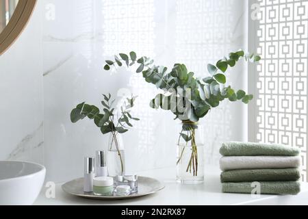 Frische Eukalyptusäste und Kosmetikprodukte auf der Arbeitsfläche im Badezimmer Stockfoto