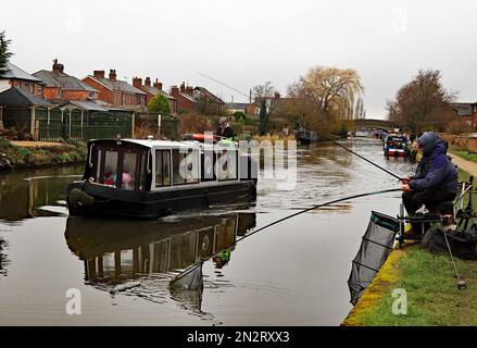 An einem kalten Wintertag landet ein Fischer einen Fang, während das lokale Ausflugsboot den Kanal von Leeds und Liverpool in Burscough entlang fährt. Stockfoto