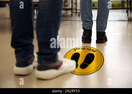 Halten Sie soziale Distanz als vorbeugende Maßnahme während des Coronavirus-Ausbruchs. Gelbes Warnschild auf dem Boden zwischen den Leuten, Nahaufnahme Stockfoto