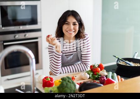 Fröhliche junge Frau aus dem Nahen Osten, die zu Hause kocht Stockfoto
