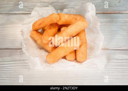 Gebratene Käsestifte in Papier auf einem weißen Holztisch Stockfoto