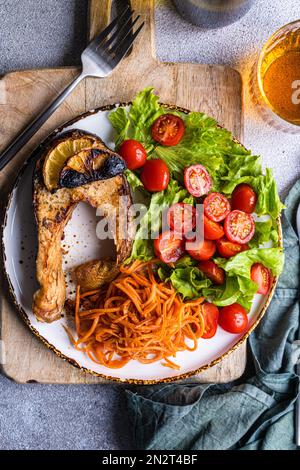 Blick von oben auf ein gegrilltes Lachssteak, Kirschtomaten, Karotten- und Salatsalat mit einem Glas Weißwein Stockfoto