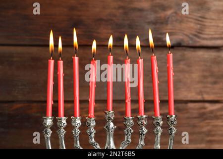 Silberne Menora mit brennenden Kerzen auf Holzhintergrund. Hanukka-Feier Stockfoto
