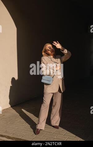 Eine Frau in einem Hosenanzug, die auf der Straße steht und ihre Augen vor der Sonne schützt, Weißrussland Stockfoto