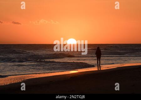 Rückansicht einer Frau, die am Strand steht und das Meer bei Sonnenuntergang betrachtet, Maspalomas Strand, Gran Canaria, Kanarische Inseln, Spanien Stockfoto