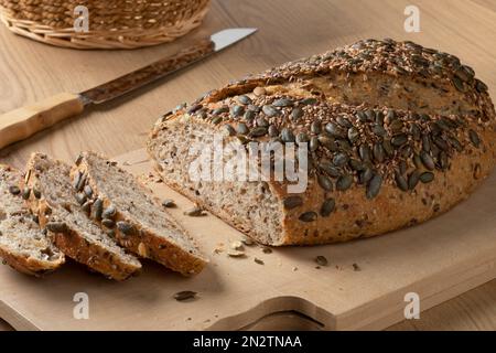 Frischer Laib und Scheiben Dinkelbrot und eine Vielzahl von Samen oben auf einem Schneidebrett Stockfoto