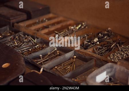 Alter Werkzeugkasten aus Holz mit Eisennägeln, Schrauben, Bolzen und Muttern. Lagerung von Baumaterialien in der Werkstatt. Sortiment an Baugeräten in Stockfoto