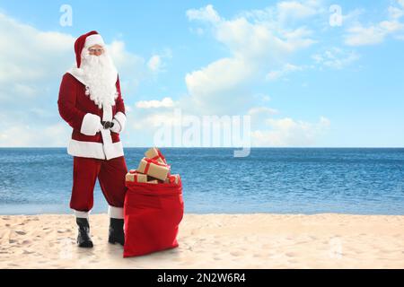 Der Weihnachtsmann in der Nähe eines Sacks voller Geschenke am Sandstrand. Platz für Text Stockfoto