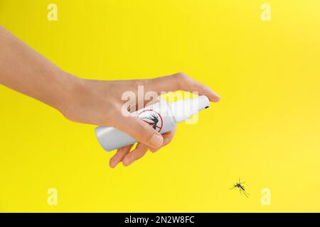 Frau, die Insektenschutzmittel auf Mücken auf gelben Hintergrund spritzt, Nahaufnahme Stockfoto