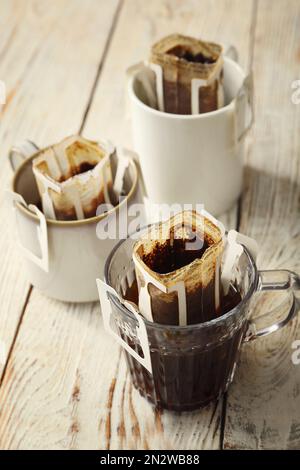 Tassen mit Kaffeebeuteln auf weißem Holztisch Stockfoto