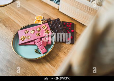 Von der Bohne bis zur Bar: Dunkle und rosafarbene Schokoriegel mit getrockneten Früchten und Nüssen auf dem Tisch. Hochwertiges Foto Stockfoto