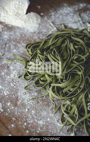 Frische Pasta. Hausgemachte italienische rohe Fettuccine-Pasta mit Spinat auf Holztisch. Hochwertiges Foto Stockfoto