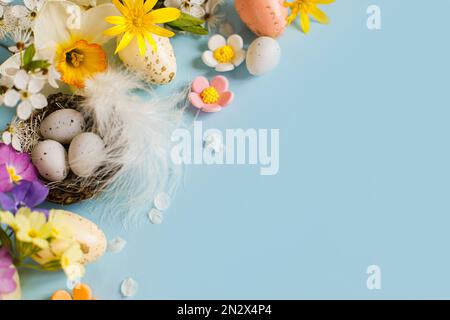 Frohe Ostern! Ostereier im Nest, bunte Blumen und blühende Kirschblüten auf blauem Hintergrund. Stilvolle festliche Vorlage mit Platz für Text. Grüß Dich Stockfoto