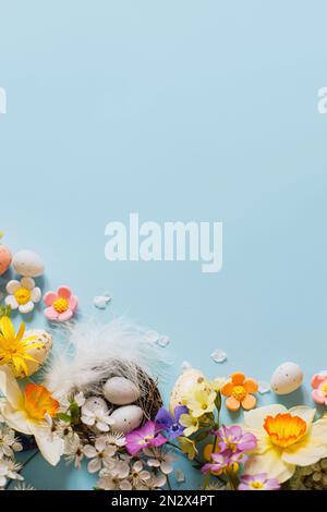 Frohe Ostern! Ostereier im Nest, bunte Blumen und blühende Kirschblüten liegen flach auf blauem Hintergrund. Stilvolle festliche Vorlage mit Platz für Tee Stockfoto