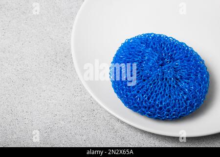 Farbenfroher Scheuerschwamm aus Kunststoff auf einer weißen Platte auf einem hellen neutralen Hintergrund. Sanftes Geschirrspülen. Hausreinigung Stockfoto