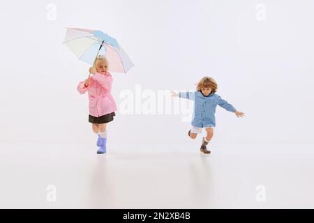 Süße Kinder, glückliche Kinder in Regenmänteln spielen, Spaß zusammen haben isoliert auf weißem Hintergrund. Konzept von Kindheit, Freundschaft, Familie, Spaß Stockfoto