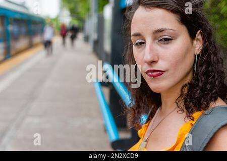 Porträt einer jungen lateinin argentinischer ethnischer Zugehörigkeit, sie ist ernst, ruhig und ruhig und schaut auf die Kamera, die draußen auf dem Bahnsteig steht, tr Stockfoto