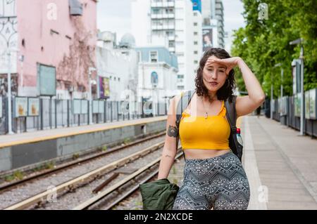 Junge lateinin argentinischer ethnischer Herkunft, trägt gelbe Kleidung und einen Rucksack. Sie ist verzweifelt, wenn sie auf der Plattform steht, mit der Hand auf ihrem Vorder Stockfoto