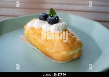 Köstlich knusprige, aufgeblasene Eclairs gefüllt mit Vanillegebäck und garniert mit Brombeeren. Stockfoto