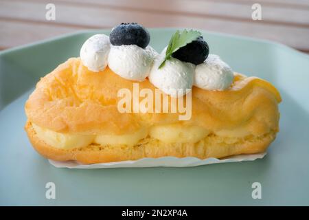 Köstlich knusprige, aufgeblasene Eclairs gefüllt mit Vanillegebäck und garniert mit Brombeeren. Stockfoto