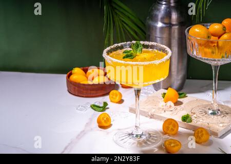 Süßer und gesalzener Kumquat margarita-Cocktail garniert mit Kumquat-Scheiben und Minze, auf Marmor und dunkelgrünen tropischen Palmen dekorierter Hintergrundkopie Stockfoto