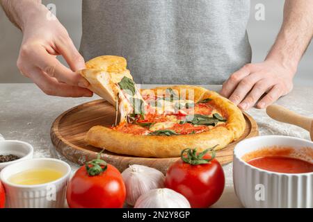 Der Prozess der Zubereitung von margarita Pizza. Männerhände, Draufsicht. Tomatenpaste mit Käse. Stockfoto