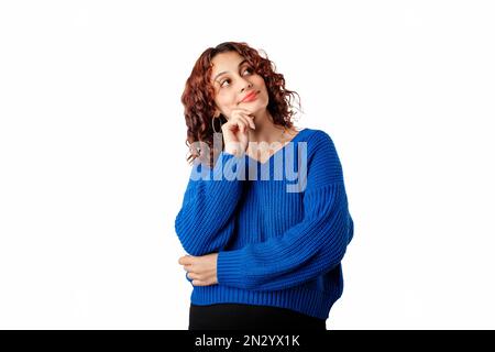 Porträt einer jungen Frau, die isoliert auf weißem Hintergrund steht, selbstbewusst und aufmerksam ist, die Hand nahe am Gesicht hält und ernsthaft leeres Kopierfeld sieht. Stockfoto