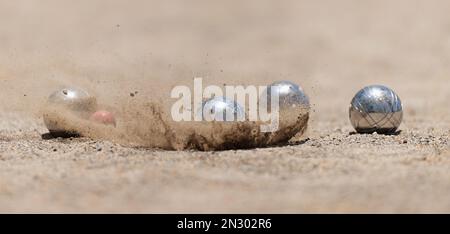 Petanque Ball Boules Schalen auf einem Staubboden, Foto beim Aufprall. Bälle und ein kleiner Holzheber Stockfoto