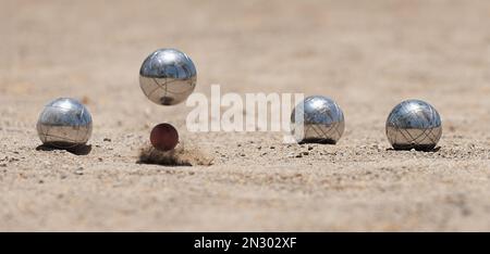Petanque Ball Boules Schalen auf einem Staubboden, Foto beim Aufprall. Bälle und ein kleiner Holzheber Stockfoto