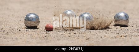 Petanque Ball Boules Schalen auf einem Staubboden, Foto beim Aufprall. Bälle und ein kleiner Holzheber Stockfoto