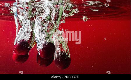 Reife Kirschen fallen ins Wasser und verursachen Spritzer und Luftblasen Stockfoto