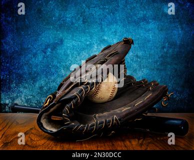 Eine Nahaufnahme von einem Baseball, einem Schläger und einem Handschuh auf einem Holztisch vor blauem Hintergrund Stockfoto