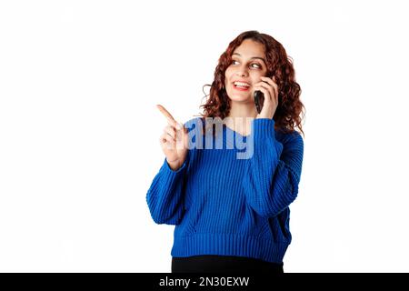 Frau steht isoliert auf weißem Hintergrund und spricht am Telefon, schaut auf den Kopierbereich und zeigt mit dem Zeigefinger. Anzeige einer Anzeige. Po Stockfoto