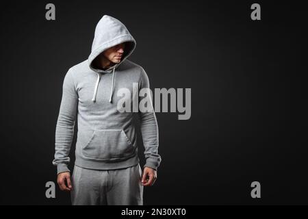 Studioporträt eines coolen jungen Mannes in Sportbekleidung, der vor dunkelgrauem Hintergrund steht. Stockfoto