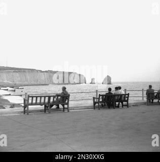 1950er, historisch, Besucher sitzen auf Bänken an der Küste von Freshwater Bay, nr Lymington, Isle of Wight, Hampshire, England, Großbritannien. Stockfoto