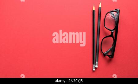 Bleistift und Brille auf rotem Hintergrund mit Kopierbereich. Stockfoto