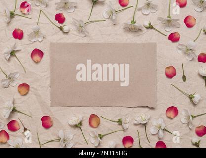 Dekorativer Rahmen aus Kirschblüten und roten Rosenblättern auf altem Kraftpapier. Vorlage für Konstruktion. Flaches Layout, Draufsicht Stockfoto