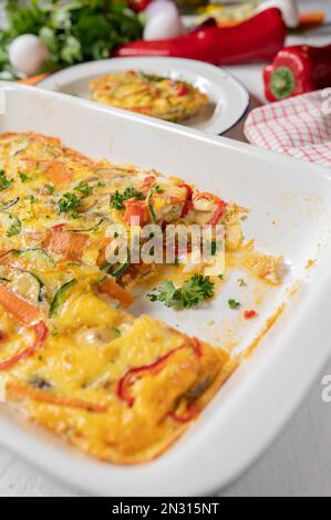 Im Ofen gebackene Frittata mit mediterranem Gemüse in einer weißen Backform auf dem Küchentisch. Stockfoto