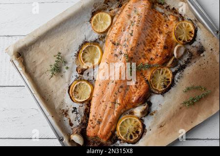 Im Ofen gebackener oder gerösteter halber Lachs gefüllt mit Zitronen-, Knoblauch- und Thymian-Marinade auf einem Backblech auf weißem Hintergrund mit Platz für Text. Flach verlegt Stockfoto