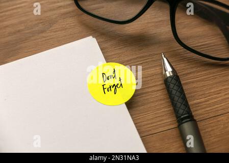 Grüner Etikettenaufkleber mit der Aufschrift „nicht vergessen“ auf einem Notizbuch mit Stift und Brille auf Holzhintergrund. Stockfoto