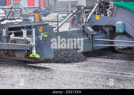 Ein industrieller Asphaltfertiger arbeitet auf Straßenarbeiten auf einer Stadtstraße und legt eine frische Asphaltschicht. Stockfoto